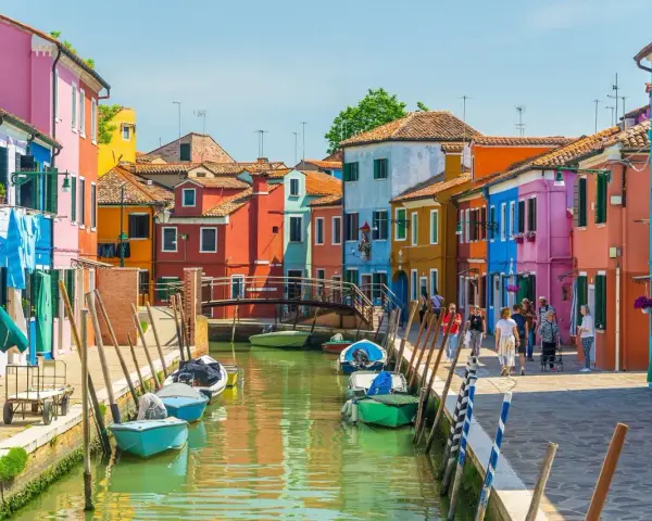 Colorate case affacciate su un canale a Venezia, con barche ormeggiate e persone che passeggiano. Le fondamenta sono un tripudio di colori vivaci.