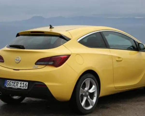 Żółta Astra GTC z tablicą rejestracyjną GG ER 116 stoi na tle morza i gór.