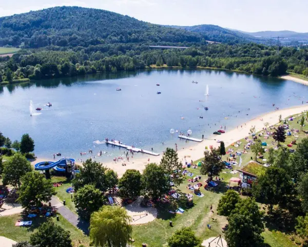 Sommerliche Idylle am Borkener See mit vielen Badegästen, Wasserrutsche und schattigen Plätzen unter Bäumen.