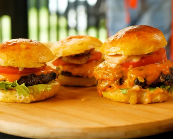 Trzy soczyste burgery z roztopionym serem, pomidorem i sałatą na desce.