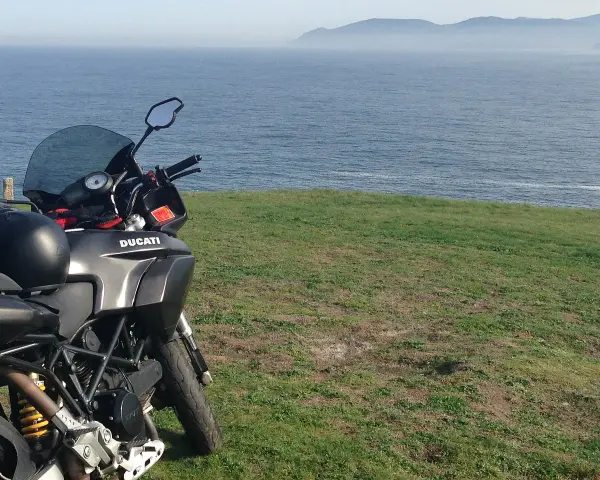 Motocykl Ducati zaparkowany na trawie z widokiem na morze. Marzenie o podróży przez Szwecję motocyklem.
