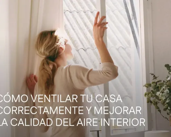 Mujer abriendo ventana para mejorar la **calidad del aire interior**. La luz del sol ilumina su cabello rubio recogido.