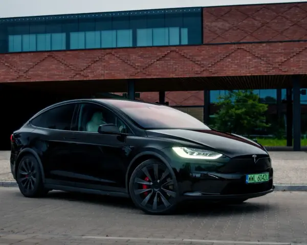 Czarny Tesla Model X zaparkowany przed nowoczesnym budynkiem z cegły.