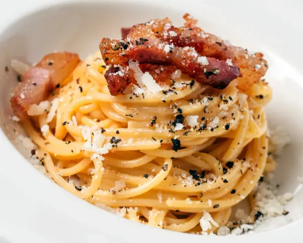 Spaghetti carbonara z chrupiącym guanciale, posypane parmezanem i czarnym pieprzem. To właśnie guanciale nadaje autentyczny smak.