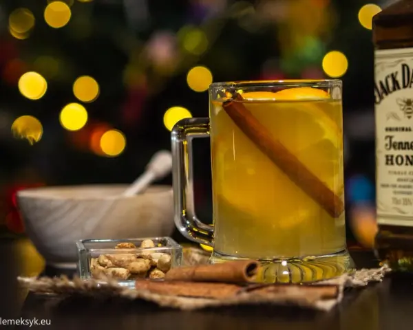 Rozgrzewający drink z Jack Daniels Tennessee Honey, z pomarańczą i cynamonem, w blasku świątecznych światełek.