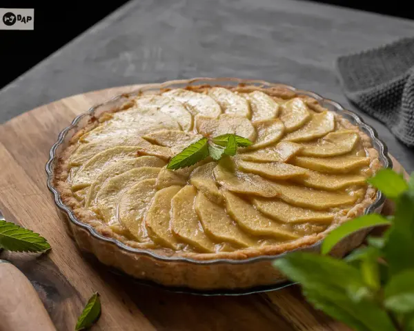 Tarta de manzana casera, con láminas de manzana doradas y una hoja de menta fresca en el centro.