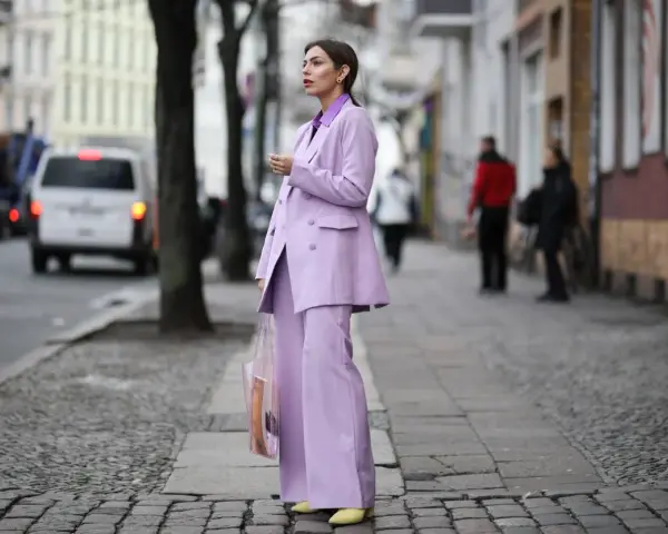 Elegancka kobieta w garniturze w kolorze liliowym, z transparentną torbą, idzie ulicą.
