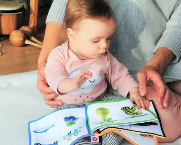 Baby lernt mit einem Stoffbuch und Musikinstrumenten. Förderung der sprachentwicklung baby.