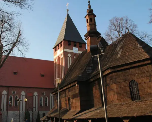 Drewniana i ceglana architektura kościołów w miasteczku śląskim, z wieżą zegarową i strzelistymi dachami, pod błękitnym niebem.