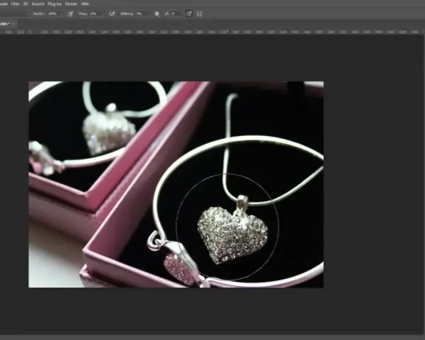 Un collier en forme de cœur orné de strass, dans une boîte rose. Un effet lumière Photoshop est appliqué pour le faire scintiller.