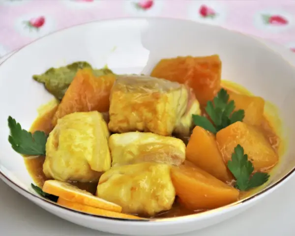 Sabroso cazon en amarillo, con trozos de pescado blanco y patatas en una salsa dorada, decorado con perejil y rodajas de limón.