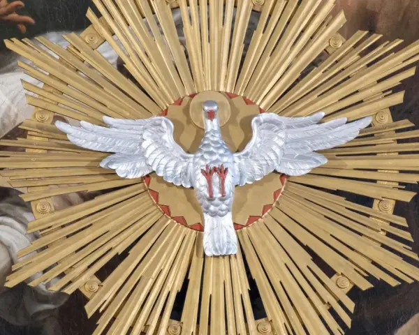 Ein silberner Taube mit ausgebreiteten Flügeln vor einem goldenen Strahlenkranz. Dies symbolisiert den Heiligen Geist und was bedeutet Pfingsten: die Ausgießung des Geistes.