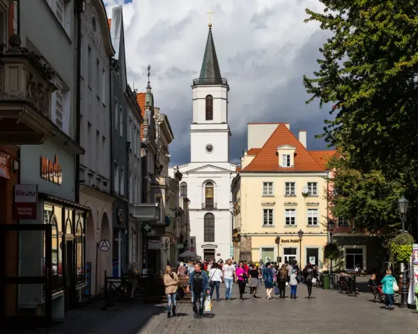 Ulica w jednym z miast na zachodzie Polski, z kościołem w tle i ludźmi spacerującymi po rynku.