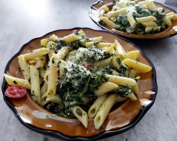 Penne z fetą i szpinakiem, posypane parmezanem. Prosty przepis na makaron ze szpinakiem i fetą.