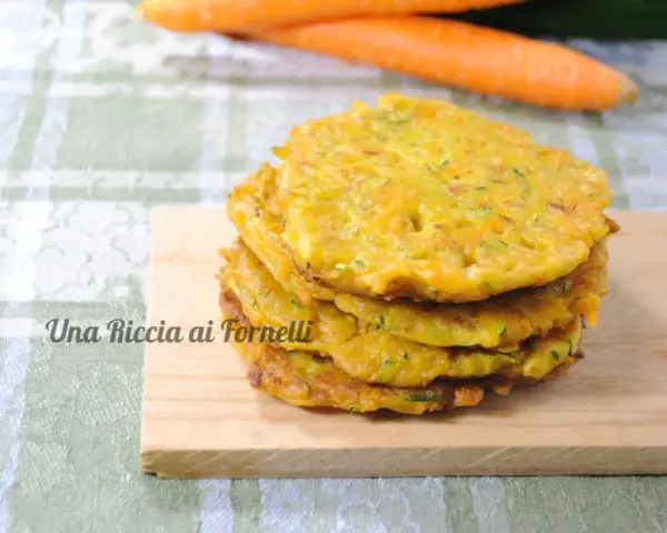 Pancakes dorati di frittata con farina di ceci, serviti su un tagliere di legno, con carote sullo sfondo.