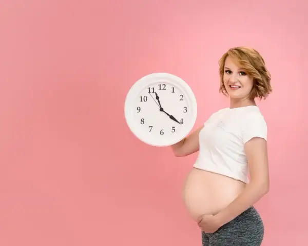 Czekasz na poród? Zegar w rękach ciężarnej sugeruje, jak przyspieszyć poród, choć to tylko symboliczne pytanie.