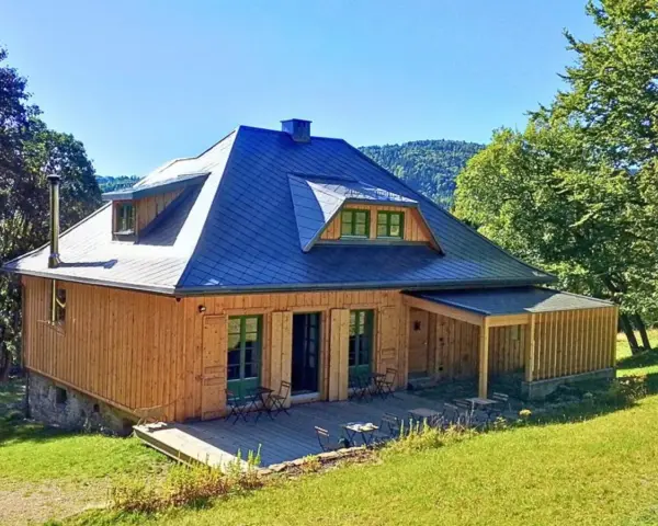 Drewniany domek z niebieskim dachem, tarasem i zielonymi okiennicami. Idealne schronisko oźna na górskim stoku.