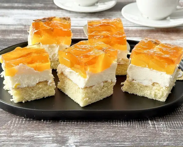 Pyszny biszkopt z galaretką bez kremu, z kawałkami owoców, na czarnym talerzu.
