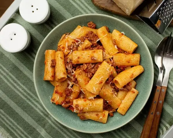 Pyszne makaron grube rurki z sosem bolońskim i parmezanem, gotowe do jedzenia.