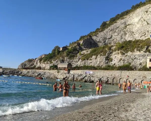 Persone si godono una giornata di sole sulla spiaggia di Erchie, con il mare azzurro e una scogliera imponente alle spalle.