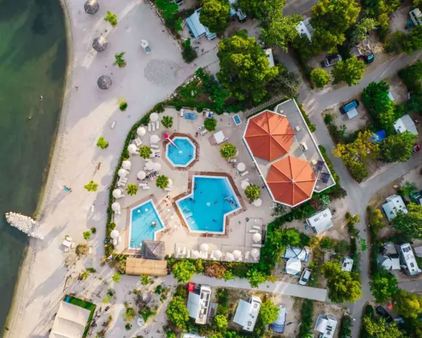 Widok z lotu ptaka na kemping z basenami i plażą. Widać tu podział na strefy: plażową, basenową i kempingową z kamperami.