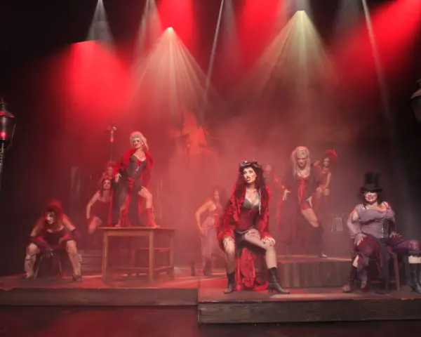Scena z musicalu "Les Miserables" z kobietami w strojach z epoki, w czerwonym świetle i dymie.
