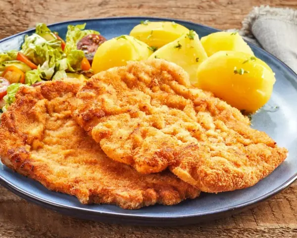 Dwa chrupiące kotlety, jeden sznycel cielęcy, drugi kotlet schabowy, podane z ziemniakami i sałatką.