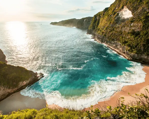 Rajska zatoka z turkusową wodą i piaszczystą plażą, idealna na wakacje na Bali. Klify porośnięte zielenią.