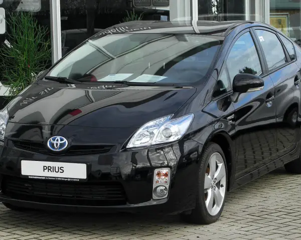Czarny Toyota Prius 3, hybrydowy samochód, lśni na tle salonu samochodowego.