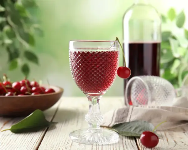 Wino z wiśni, które można zrobić z tych owoców. Kieliszek pełen rubinowego napoju, obok miska świeżych wiśni.
