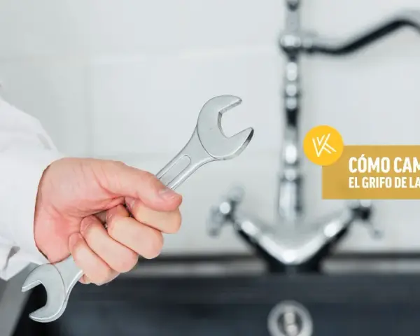 Mano con llave inglesa lista para instalar grifo cocina. Texto: "Cómo cambiar el grifo de la cocina".