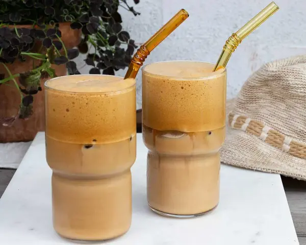 Två glas med iskaffe, perfekt för ett somrigt iskaffe recept. Med tjockt skum och isbitar.