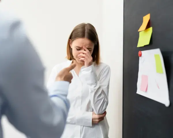 Mujer llora mientras un colega la señala, sufriendo acoso laboral.