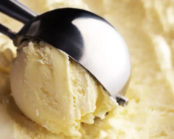 Un cucchiaio raccoglie una pallina di cremoso gelato con yogurt greco, pronto per essere gustato.