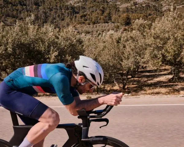 Cyclist pushing hard on a road bike, focused on a VO2 max workout amidst a scenic, tree-lined landscape.