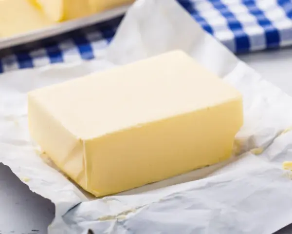 Kostka masła na papierze, obok niebiesko-biała ściereczka. Czy masło można mrozić? Tak, można je zamrozić, by zachować świeżość.