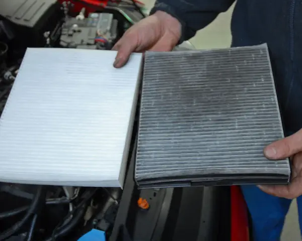 Hands hold a new white air filter next to a dirty, used one, ready to replace air filter in car.