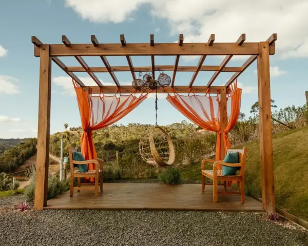 En vacker träpergola med orange draperier och hängstol. Perfekt för att bygga pergola på altan och njuta av utsikten.