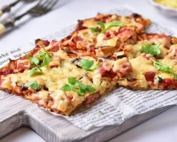 Pyszna pizza na spodzie z kalafiora keto, z szynką i serem, udekorowana świeżą pietruszką.