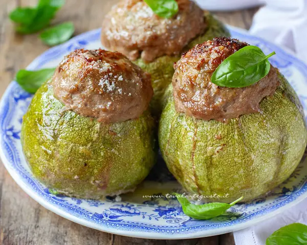 Zucchine tonde ripiene, un piatto gustoso del menù di Benedetta, servite su un piatto blu e bianco con basilico fresco.