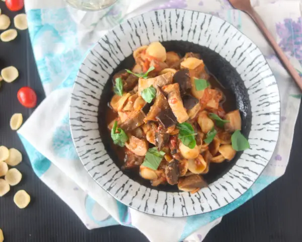 Orecchiette con pesce spada e melanzane, un piatto saporito e colorato, guarnito con basilico fresco.