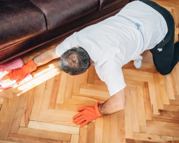 Man in orange gloves cleaning wooden floor with a pink cloth.