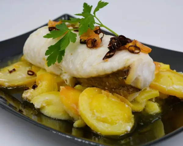 Rape con patatas, un plato delicioso con pescado blanco tierno y patatas doradas, decorado con perejil fresco y crujientes trozos de ajo frito.