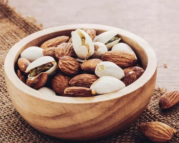 Un bol en bois rempli d'amandes et de pistaches, une liste d'oléagineux parfaite pour une collation saine.