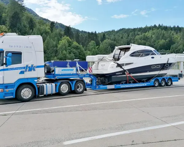 Ein LKW transportiert ein luxuriöses Boot auf einem Spezialanhänger. Die Yacht ist sicher auf dem Anhänger befestigt, bereit für den Transport über Land.