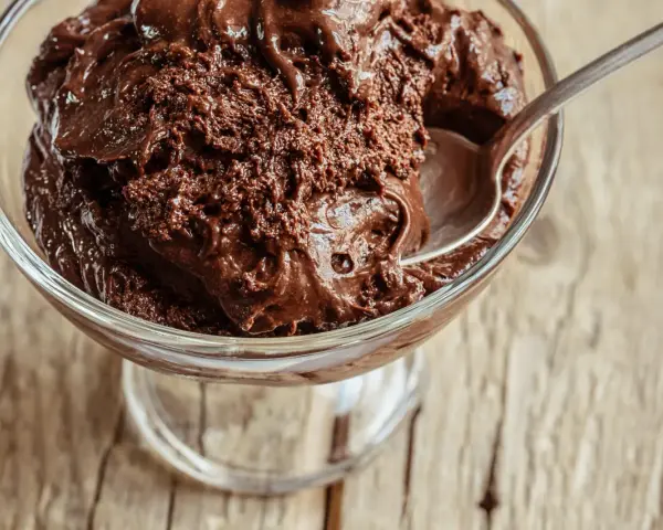 Une cuillère s'enfonce dans une coupe de mousse au chocolat au lait onctueuse, prête à être dégustée.