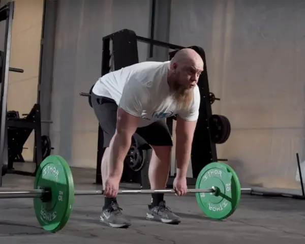 Man med skägg utför raka marklyft med hantlar i ett gym.
