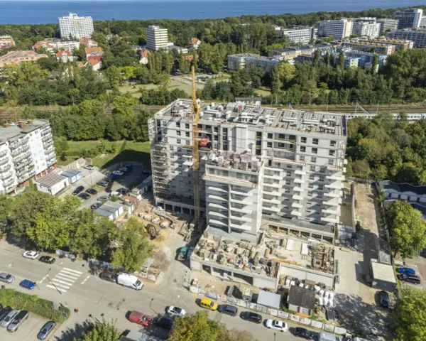 Budowa bloku mieszkalnego w Kołobrzegu. Widok z lotu ptaka na plac budowy, dźwig, samochody i okoliczne budynki. Ceny mieszkań Kołobrzeg mogą być różne.