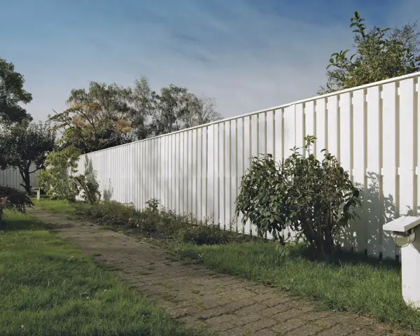 Vit staket med stående panel, en stenlagd gång och grönskande trädgård. Perfekt för att bygga plank stående panel.