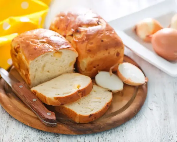 Zwiebelbrot rezept: goldbraune Brote mit Zwiebeln, angeschnitten, daneben Zwiebeln und ein Messer.